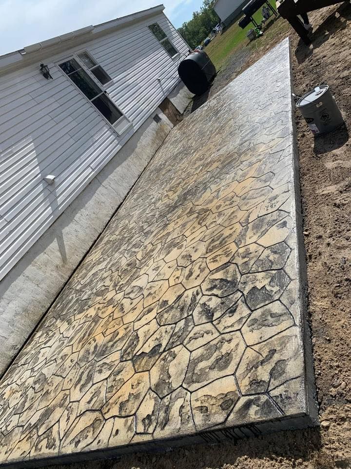 Stamped concrete patio beside a white house, with a cracked section and a trash can near the wall