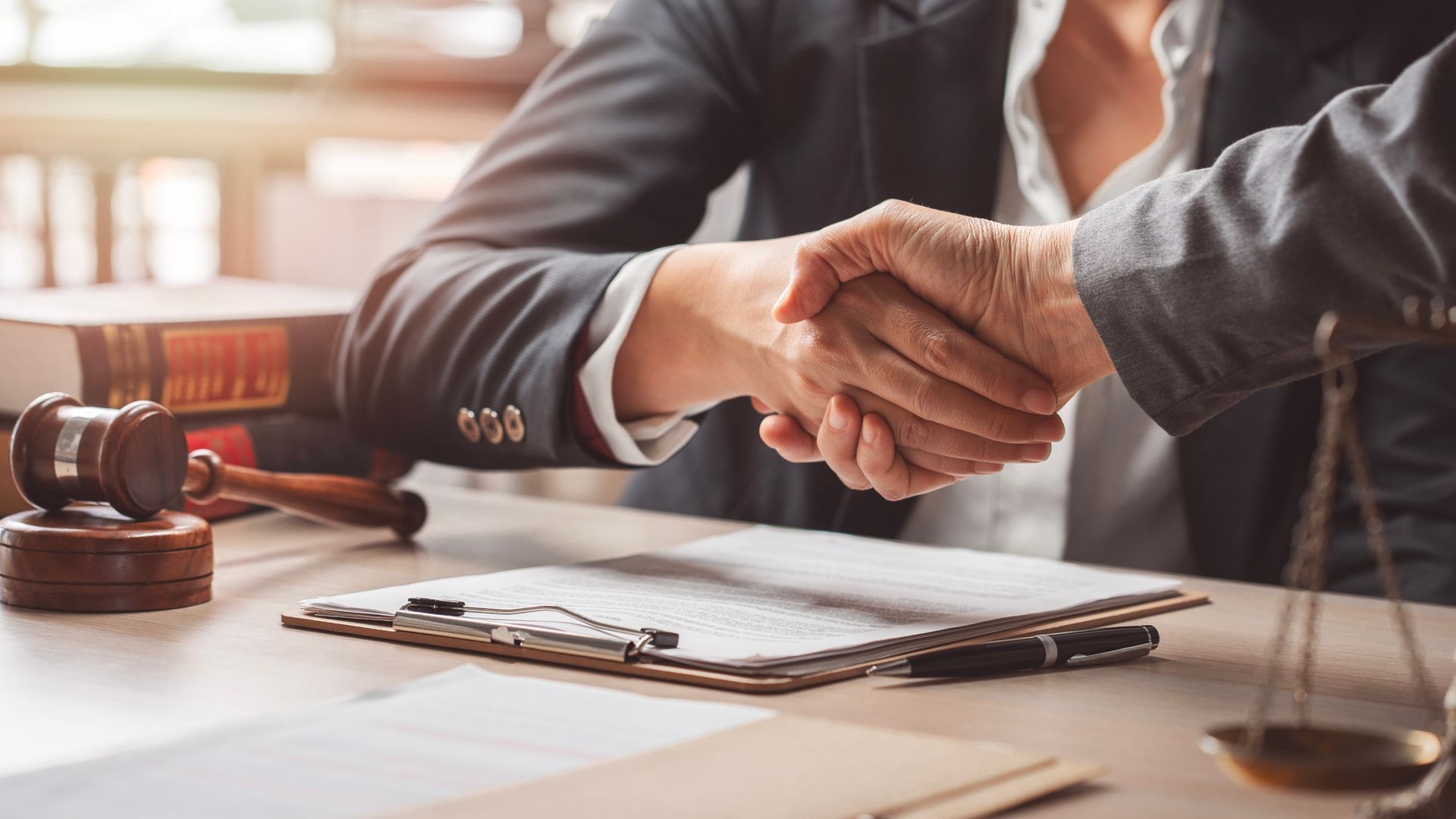 Handshake across desk with gavel and scales, symbolizing justice and legal agreement