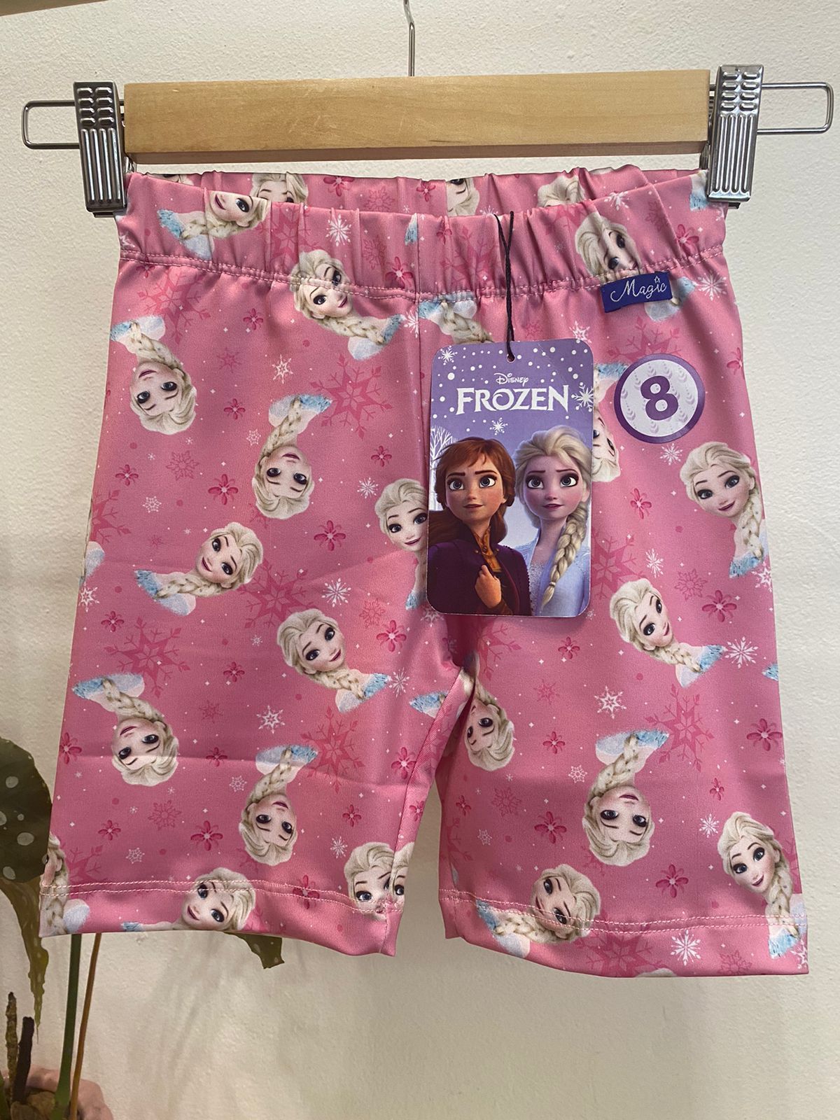 Pantalones cortos rosas con temática de Frozen en una percha con una etiqueta de talla 8.