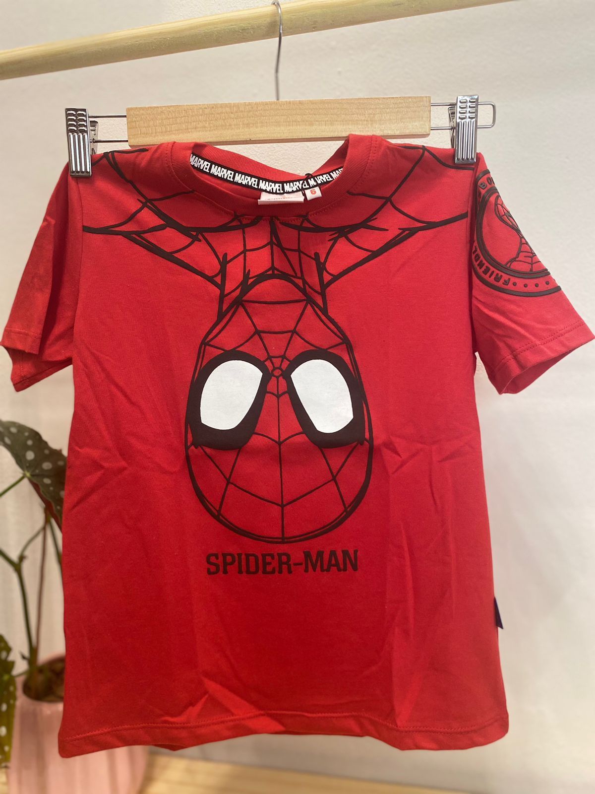 Camiseta roja de Spider-Man colgada en una percha de madera. La cara de Spider-Man destaca en la parte delantera.