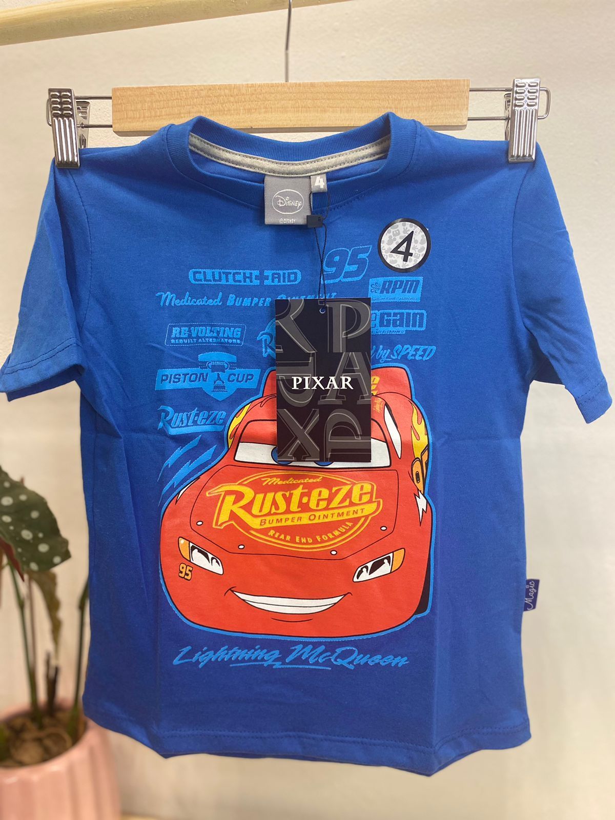 Camiseta azul con el gráfico de Rayo McQueen y el logo "Rust-eze". Tiene una etiqueta con el número "4".