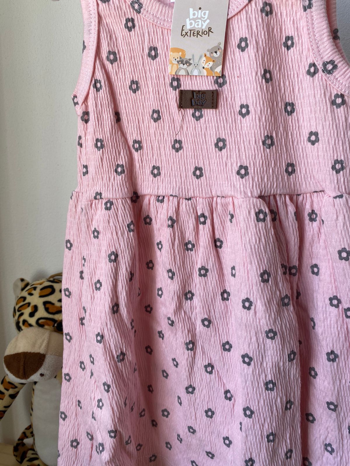 Vestido infantil sin mangas de color rosa con estampado de estrellas, colgado en una percha blanca.