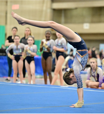 A woman is helping a young girl do a handstand on a blue mat.