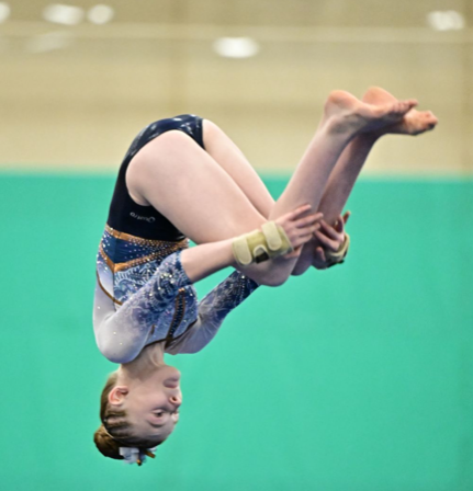 A woman is helping a young girl do a handstand on a blue mat.