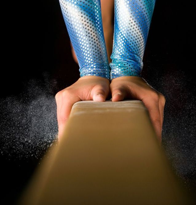 A gymnast is sitting on a balance beam covered in chalk.