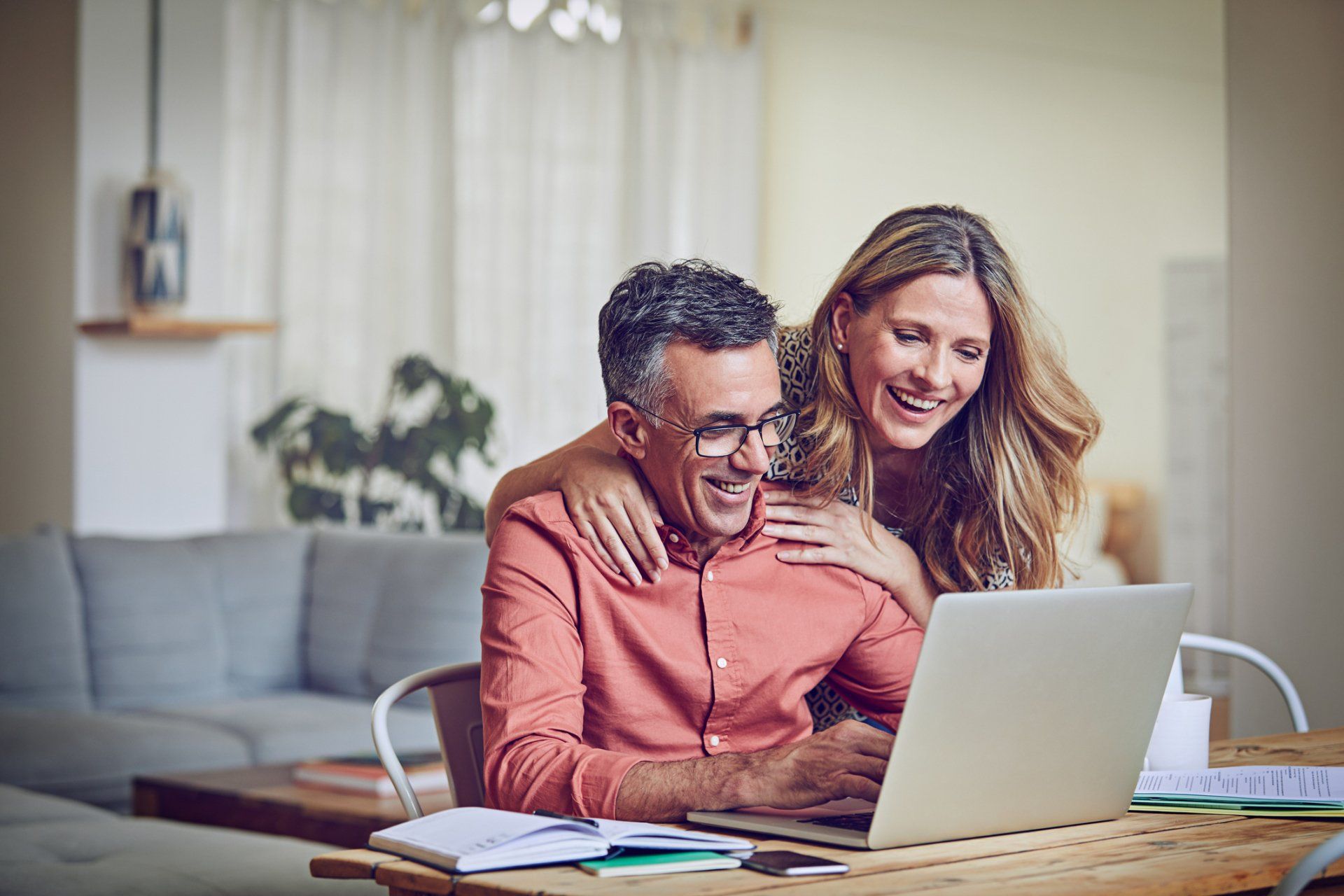 A man and a woman are sitting at a table looking at a laptop computer.