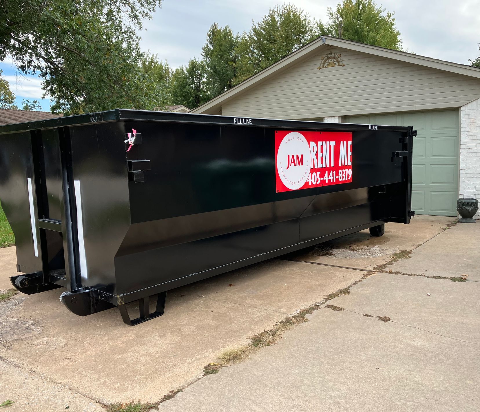 A dumpster is parked in a driveway in front of a house.