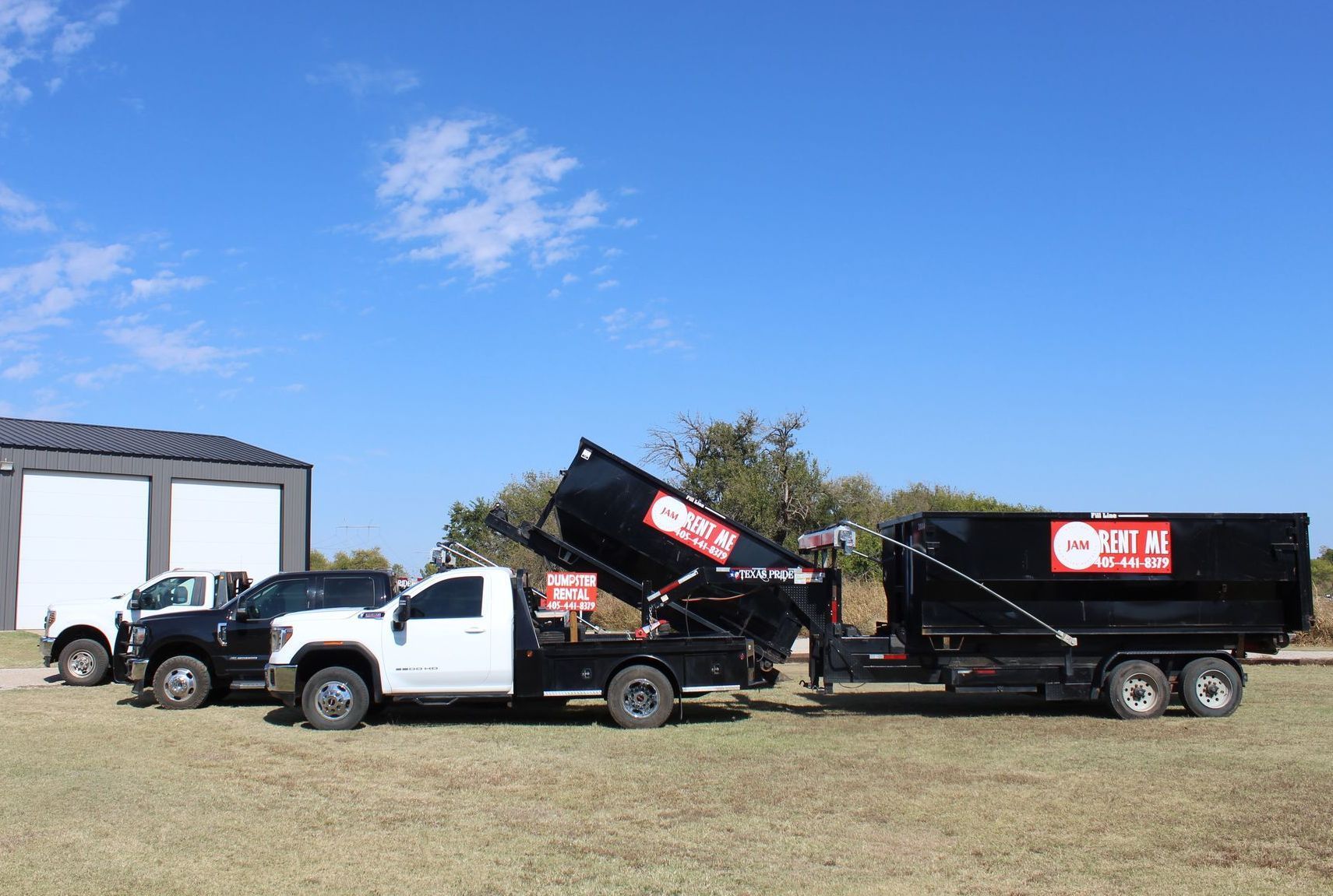 Two dump trucks are parked next to each other in a grassy field.