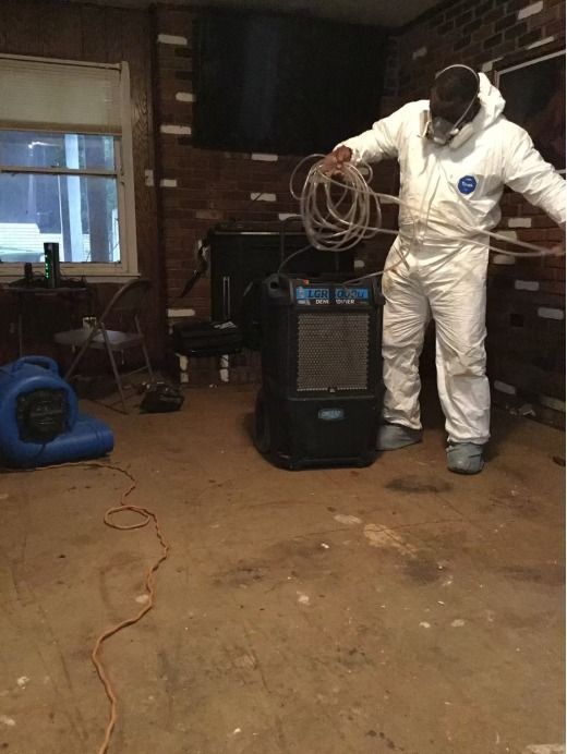 Person in protective suit with equipment in a room, possibly after water damage.