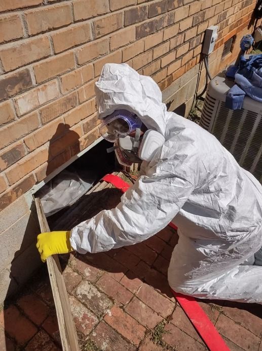 Person in protective suit kneeling by a brick wall, entering an opening. Red hose visible.
