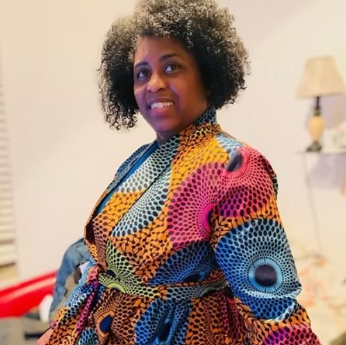 Woman in colorful patterned wrap dress smiles indoors.
