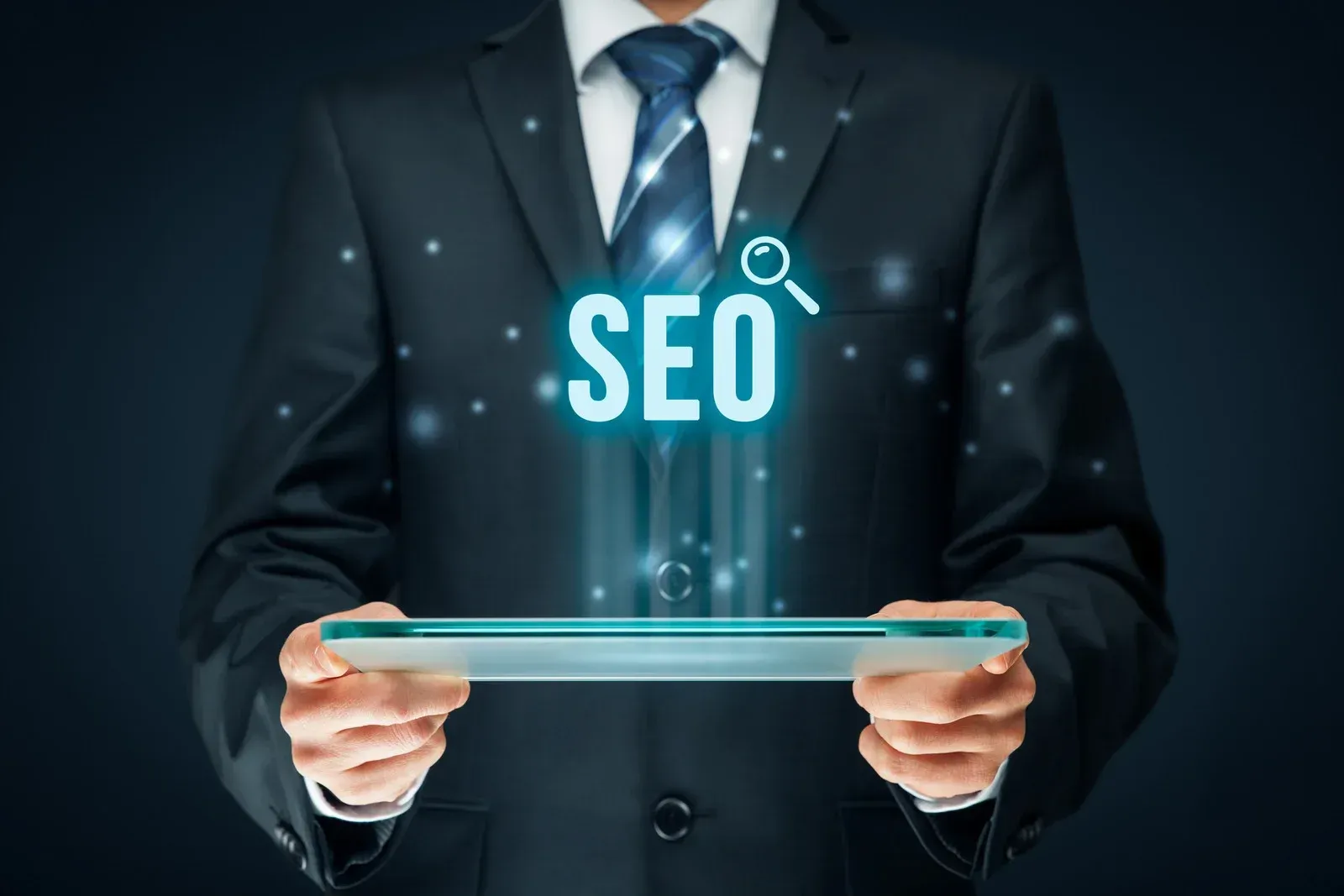 A man in a suit and tie is holding a tablet with the word seo coming out of it.