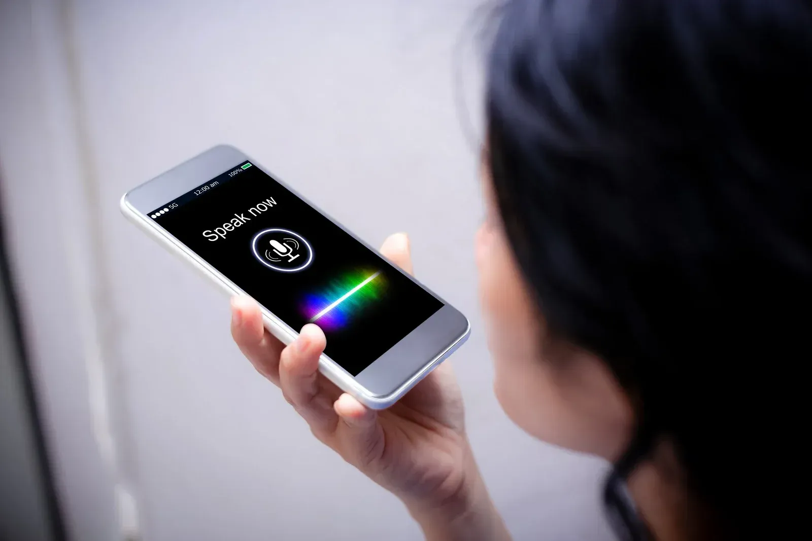 Woman holding smartphone, using voice assistant. Screen shows sound wave and active microphone icon.