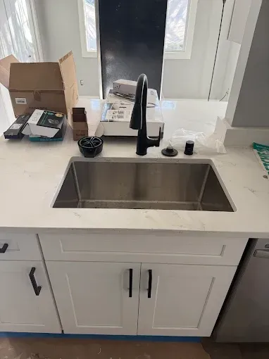 White kitchen sink with black faucet and countertop items, viewed from above.