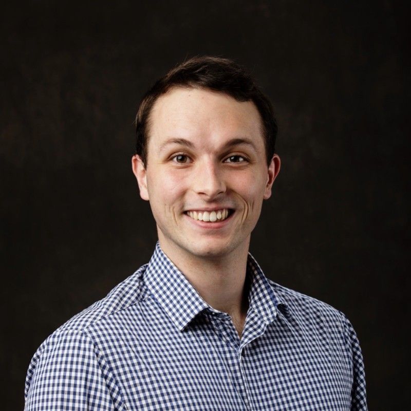 Smiling man in blue checkered shirt against a dark background.