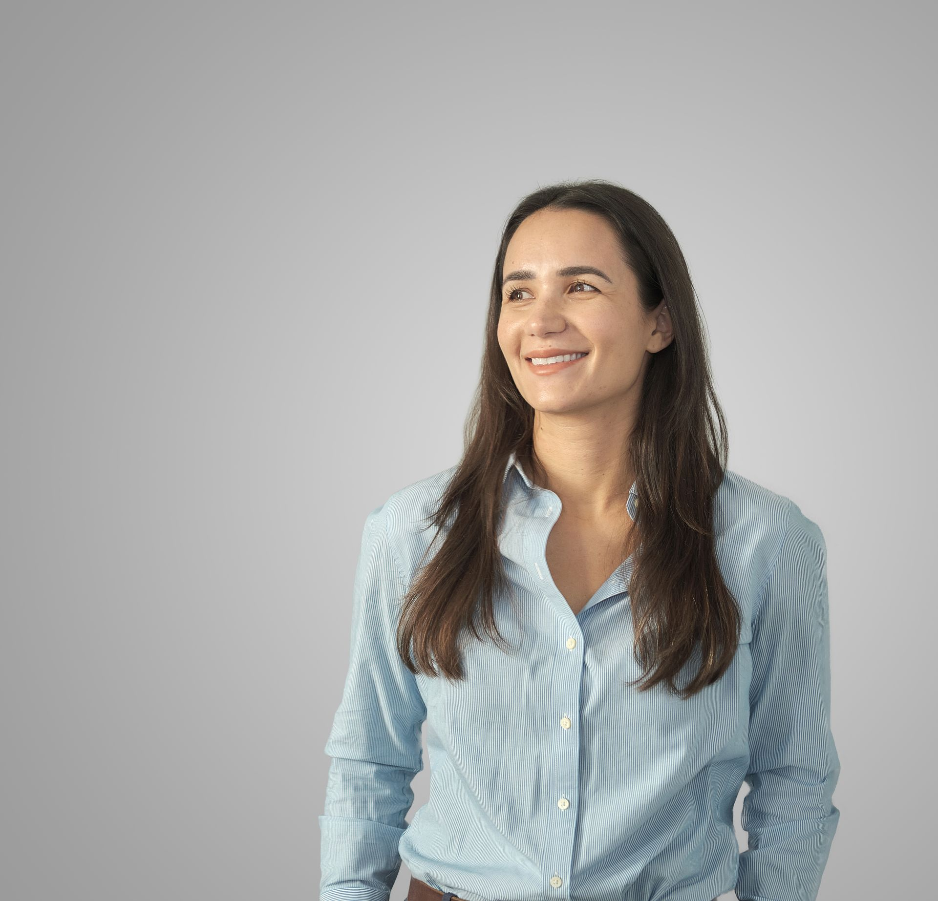 Woman with long brown hair, wearing a beige sweater, looking directly at the camera, in front of colorful artwork.