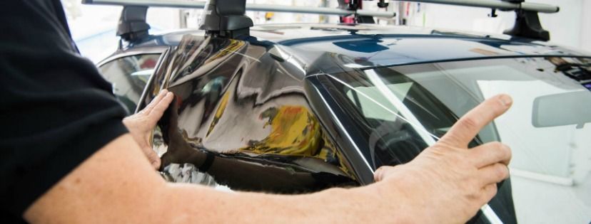 A person applying film to a car windshield. They are holding the film in place.