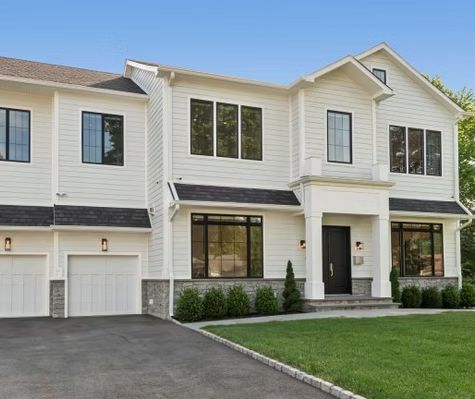 A large white house with two garages and a lush green lawn.