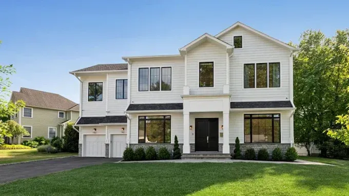 A large white house with a black door is sitting on top of a lush green lawn.