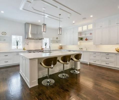 A kitchen with white cabinets , stainless steel appliances , hardwood floors and a large island.