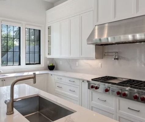 A kitchen with white cabinets , a stove top oven , a sink , and a window.