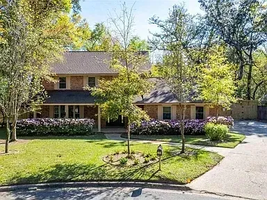 A large brick house with a lush green lawn and trees in front of it.
