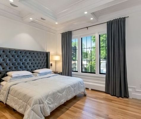 A bedroom with a king size bed , gray curtains and a large window.
