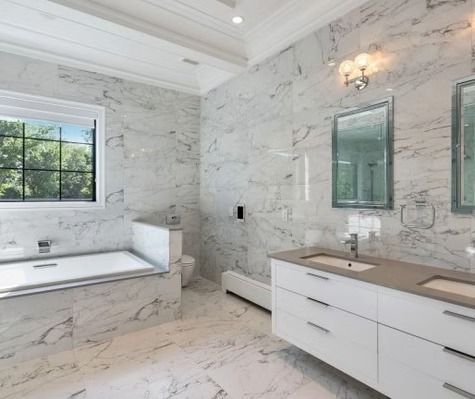 A bathroom with marble walls , two sinks , a tub and a window.