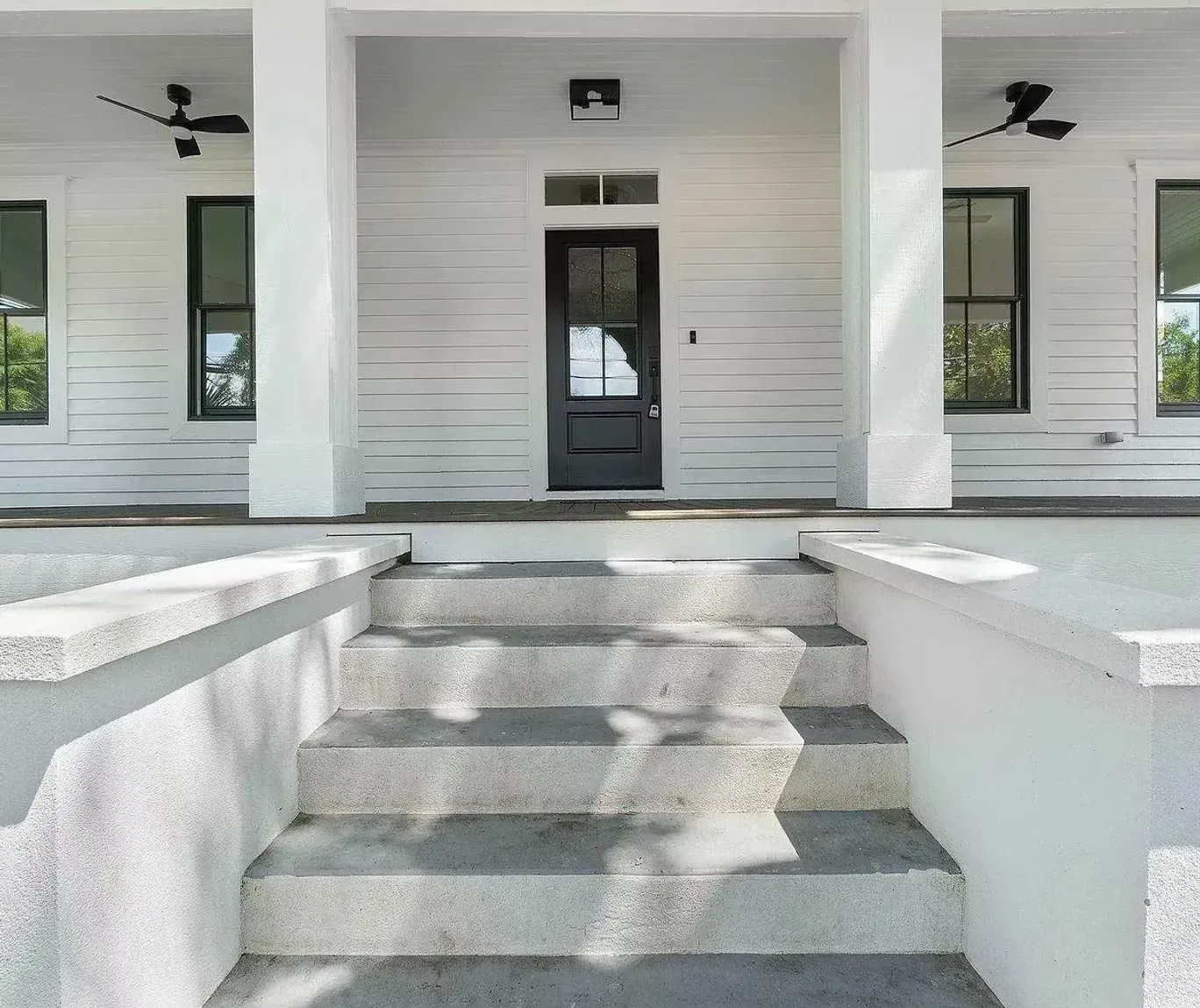 A white house with a black door and stairs leading up to it.