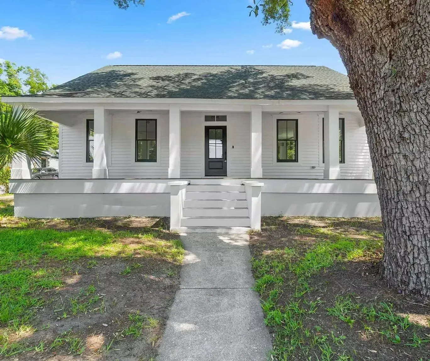 A white house with a porch and a tree in front of it.