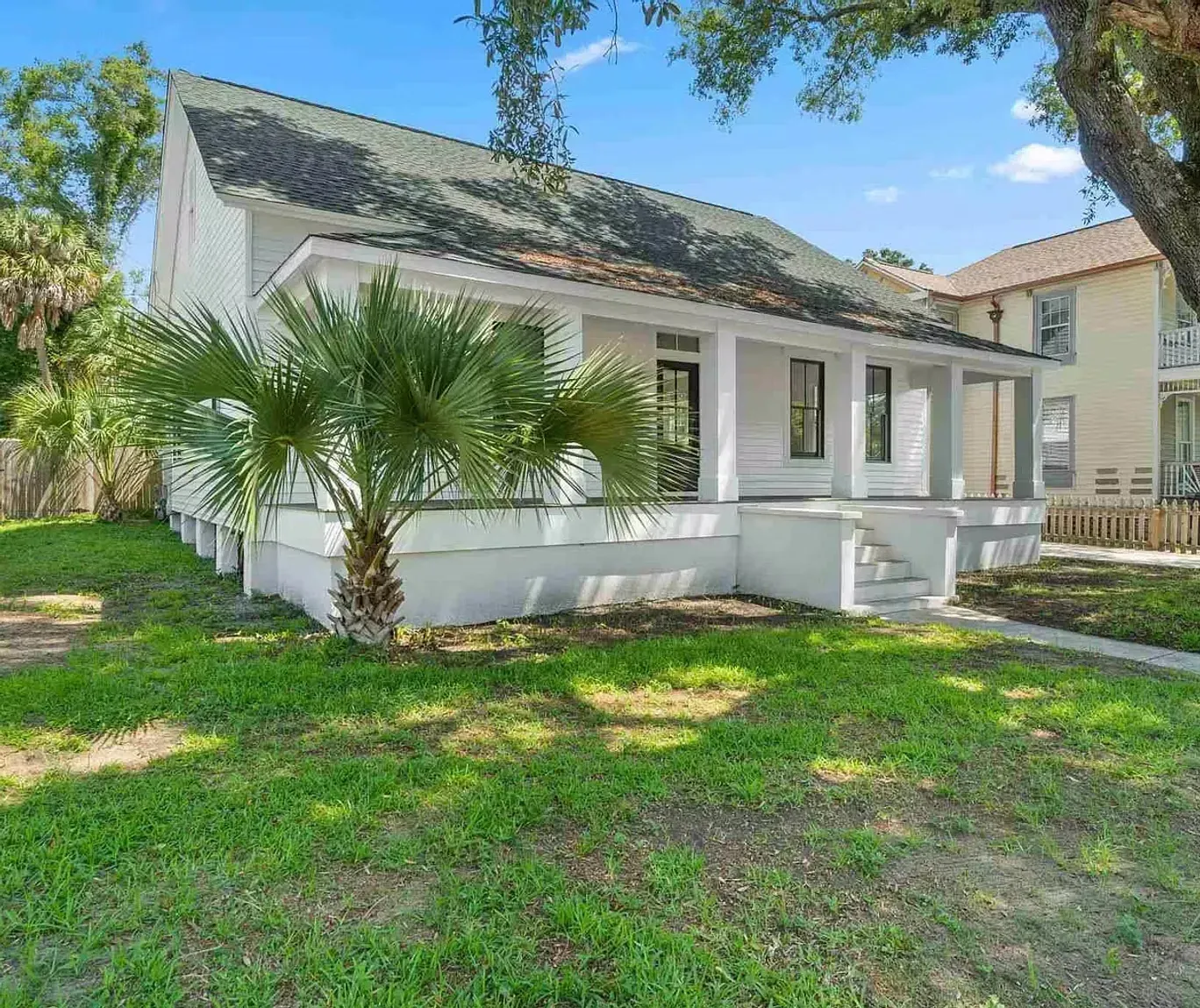 A white house with a large porch and a palm tree in front of it.