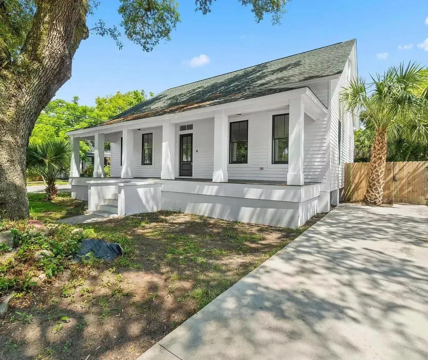 A white house with a porch and a tree in front of it.
