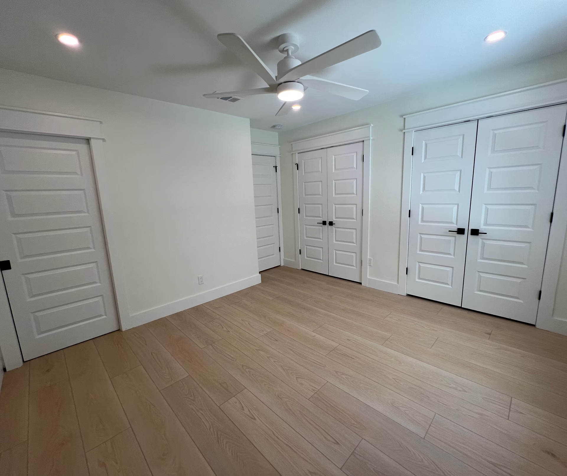 A bedroom with hardwood floors , white doors and a ceiling fan.