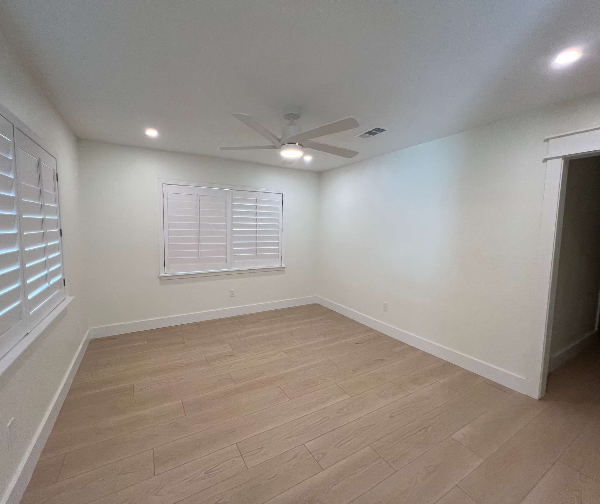 An empty bedroom with hardwood floors , white walls and a ceiling fan.