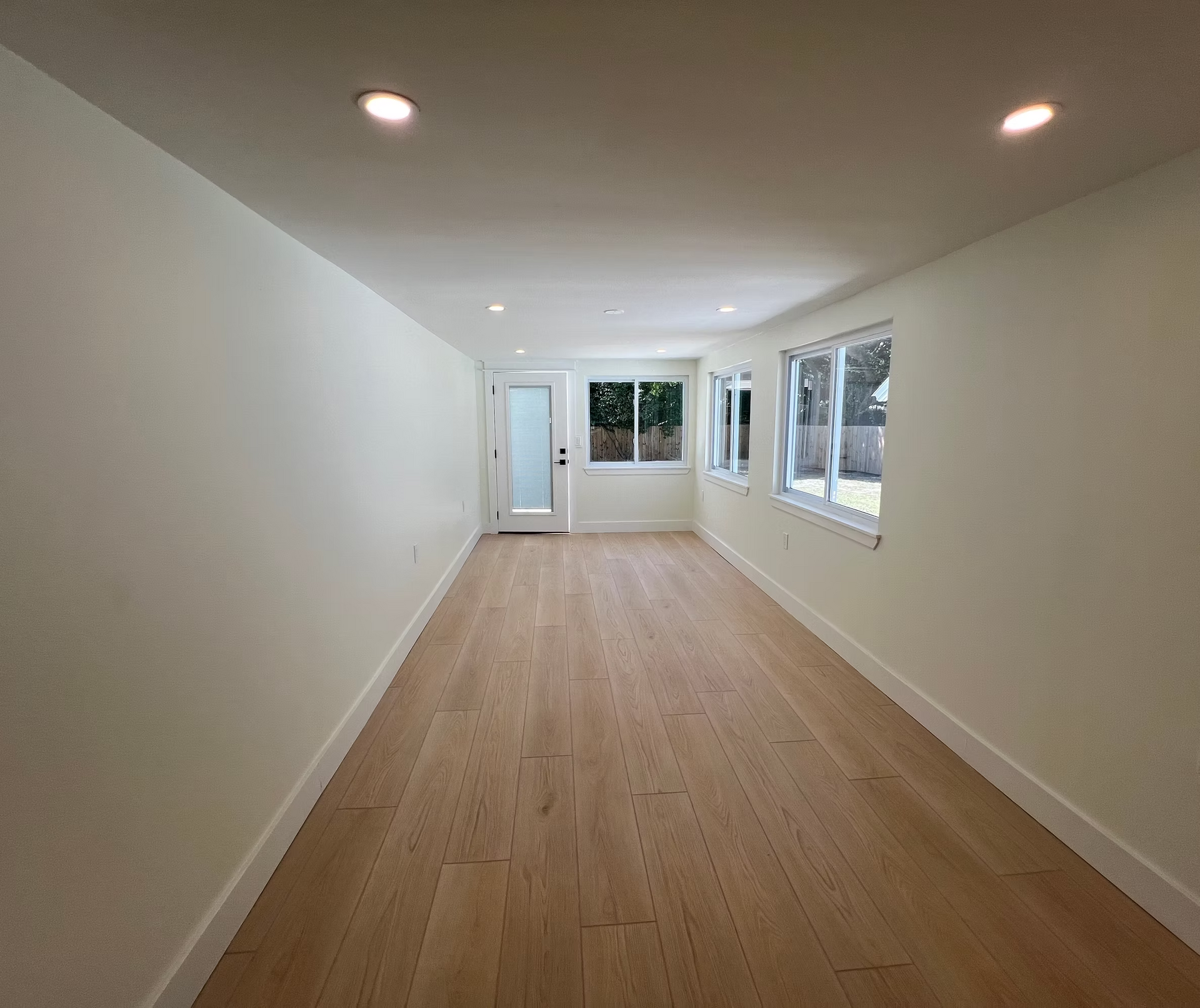 A long empty room with hardwood floors and white walls.