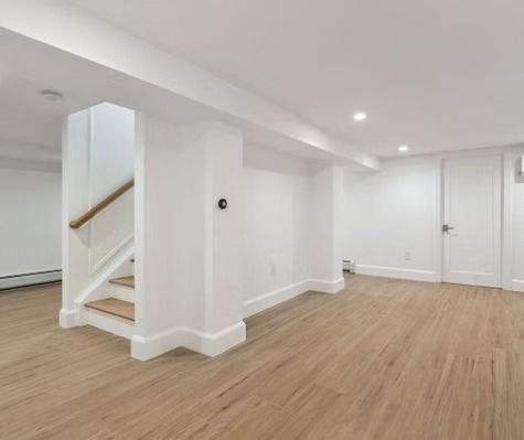 A basement with hardwood floors , white walls and stairs.