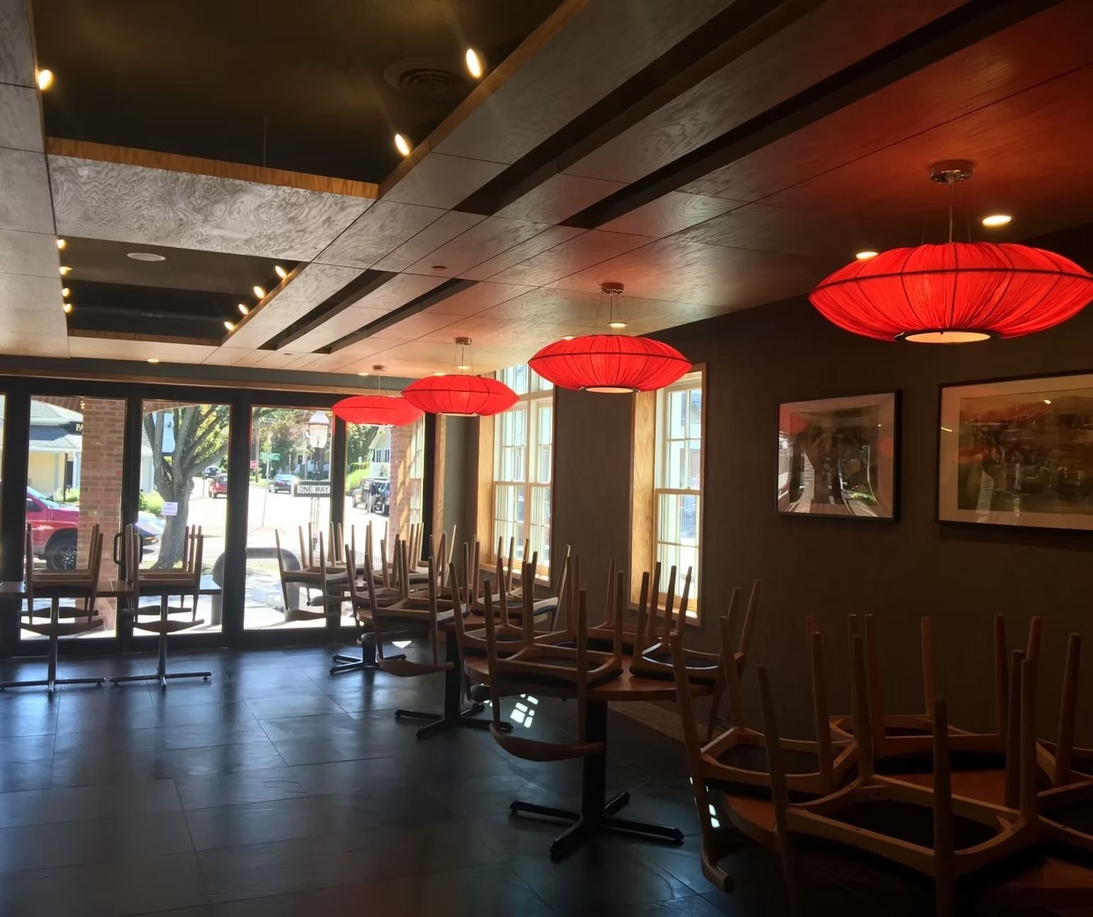 A restaurant with tables and chairs empty and red lanterns hanging from the ceiling
