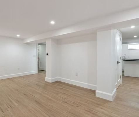 An empty basement with hardwood floors and white walls.