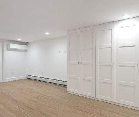 An empty room with hardwood floors and white cabinets.