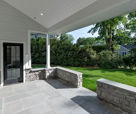 There is a porch with a stone wall and a lawn in the background.