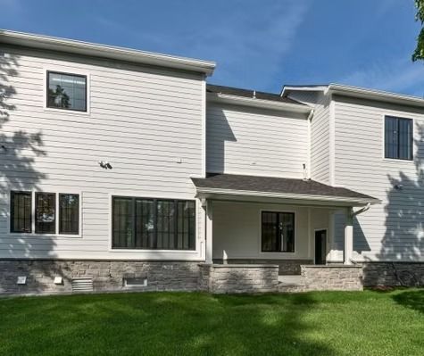 The back of a large white house with a porch and a lot of windows.
