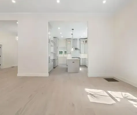 An empty room with hardwood floors and a kitchen in the background.