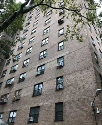 A tall brick building with a lot of windows is surrounded by trees.