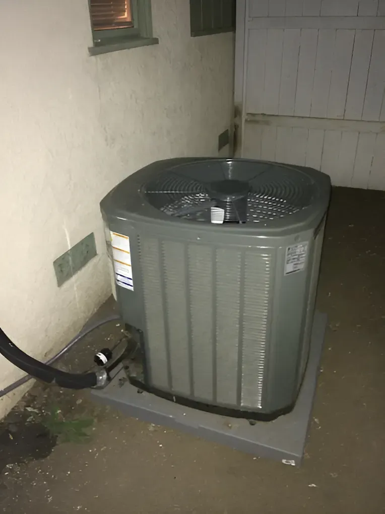 Gray air conditioning unit on a platform next to a white wall.