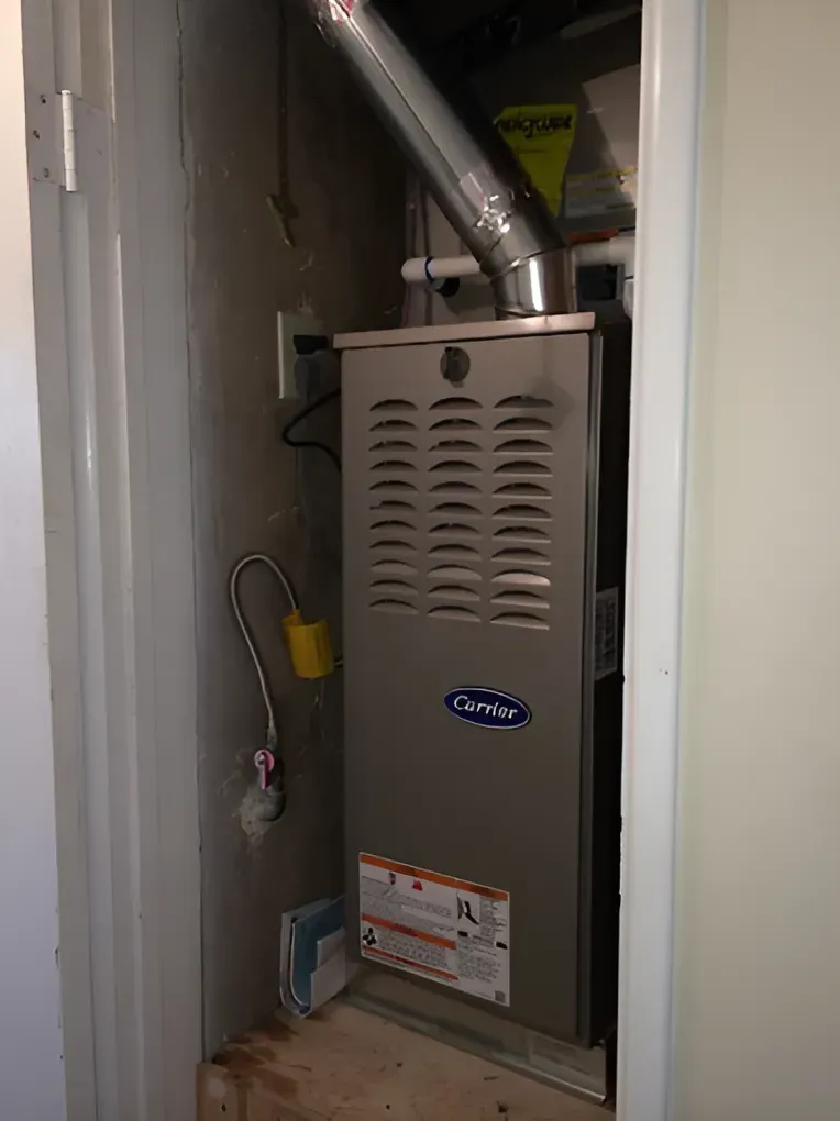 A Carrier furnace inside a utility closet with a vent pipe and attached gas line.