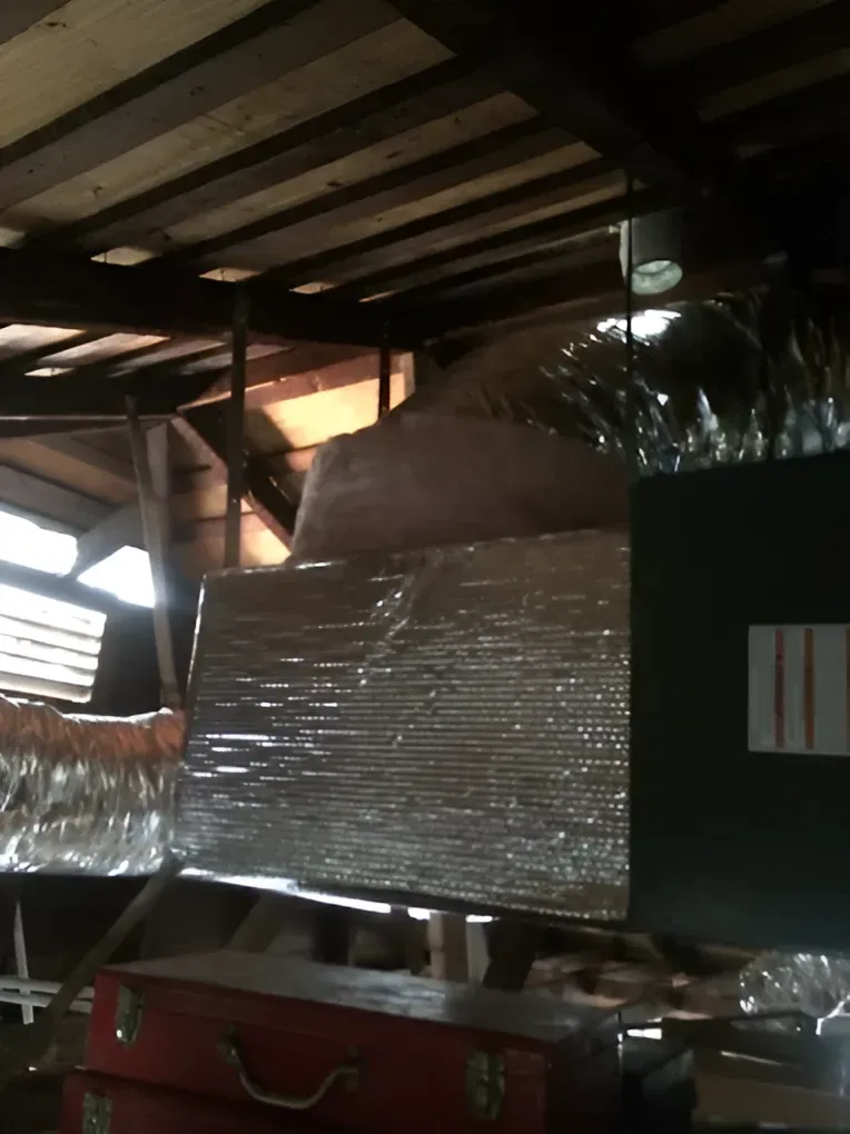 Attic with insulation, ductwork, and a toolbox. Sunlight streams through a window.