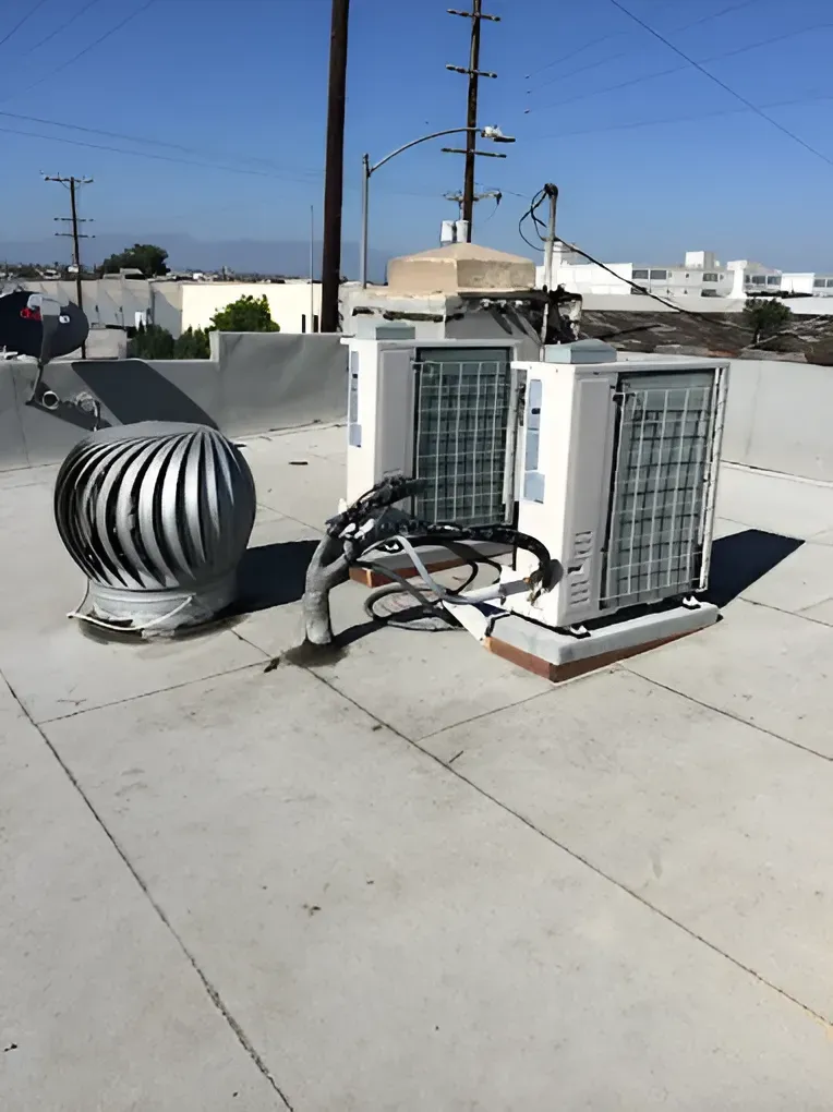 Rooftop with air conditioning units, a vent, and electrical equipment under a bright blue sky.