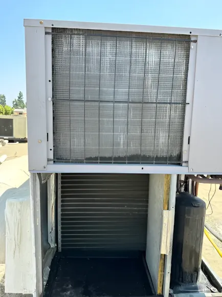 A dirty air conditioning unit on a rooftop with a grimy filter and metal coils.