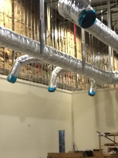 HVAC ductwork wrapped in silver insulation, suspended from ceiling in a construction site.