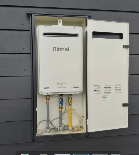 A Rinnai tankless water heater installed in an outdoor, white cabinet. The cabinet door is open.